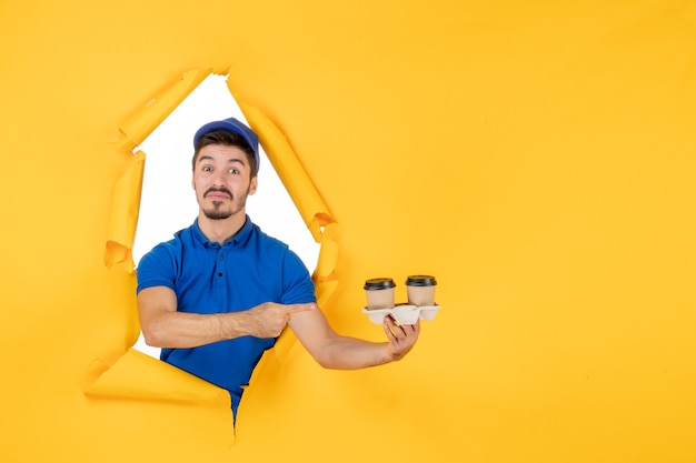 Free Photo front view male courier in blue uniform holding coffee cups on the yellow space