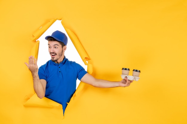 Free photo front view male courier in blue uniform holding coffee cups on yellow space