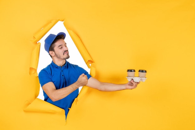 Free Photo front view male courier in blue uniform holding coffee cups on yellow space