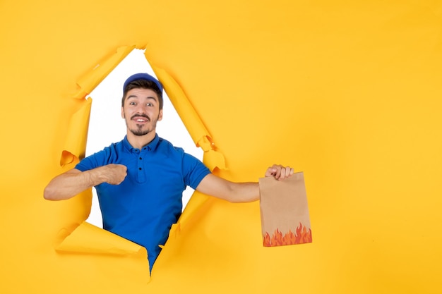 Free Photo front view male courier in blue uniform holding food package on yellow space