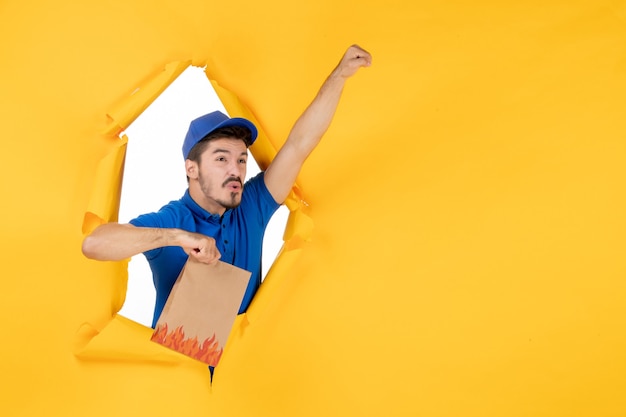 Front view male courier in blue uniform holding food package on yellow space