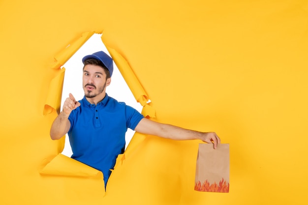 Free Photo front view male courier in blue uniform holding food package on yellow space