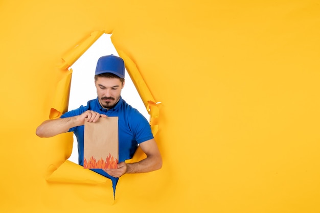 Free Photo front view male courier in blue uniform with food package on a yellow space