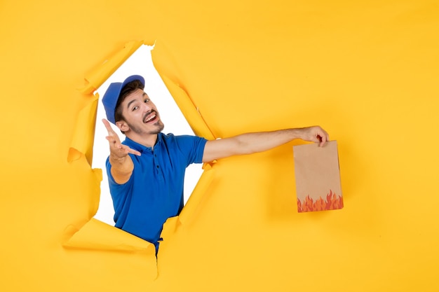 Free Photo front view male courier in blue uniform with food package on the yellow space