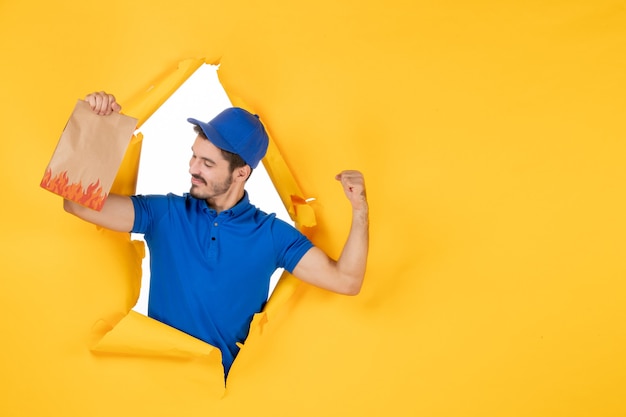 Free Photo front view male courier in blue uniform with food package on yellow space