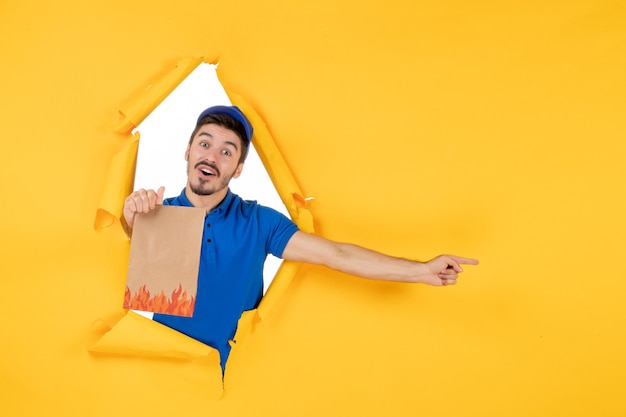 Front view male courier in blue uniform with food package on yellow space