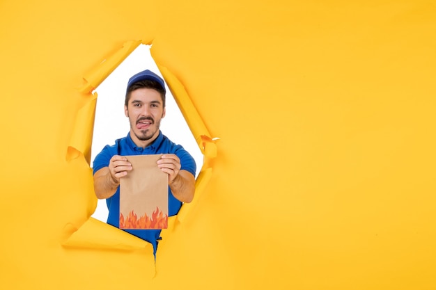 Free photo front view male courier in blue uniform with food package on yellow space