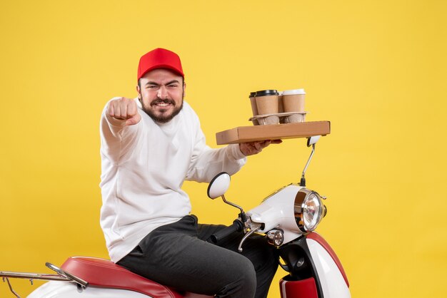 Front view of male courier holding delivery coffee and food on a yellow wall