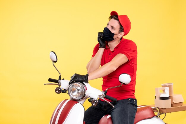 Front view male courier in red uniform and mask on a yellow 