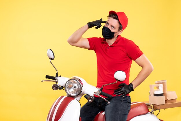 Front view male courier in red uniform and mask on yellow 