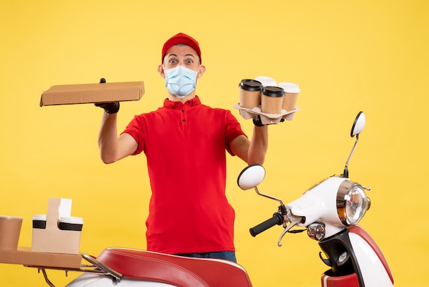 Front view male courier in uniform with coffee and food box on yellow pandemic service work covid uniform job virus colors