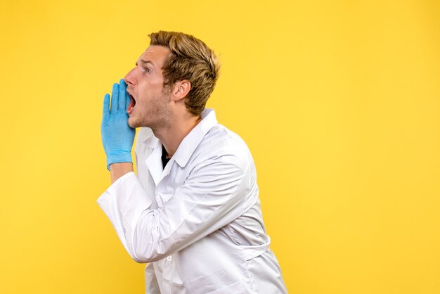 Front view male doctor calling loudly on yellow background covid- human emotion medic