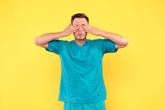 Free photo front view of male doctor covering his eyes on yellow wall