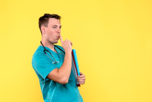 Front view of male doctor holding analyzes on yellow wall