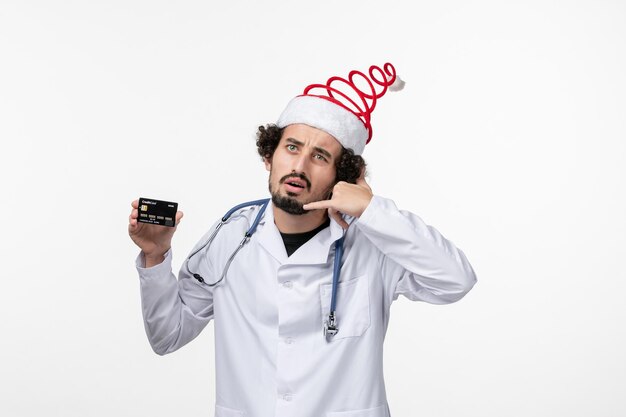 Front view of male doctor holding bank card on white wall