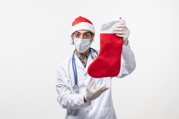 Front view male doctor holding big holiday sock on the white wall covid virus holiday