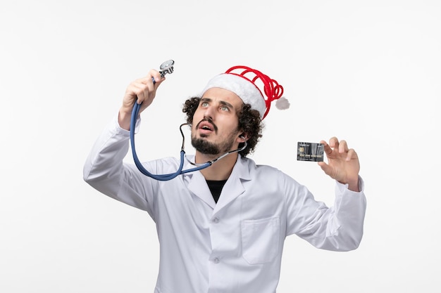 Front view of male doctor holding black bank card on a white wall