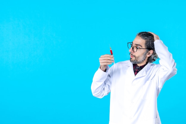 Front view male doctor holding injection on a blue