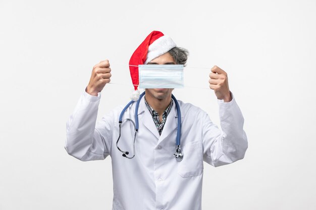 Front view male doctor holding mask on white wall new year holiday virus covid