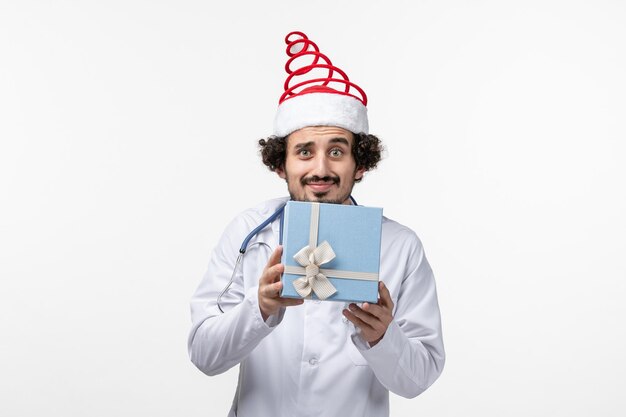 Front view of male doctor holding present on a white wall