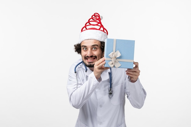 Front view of male doctor holding present on white wall