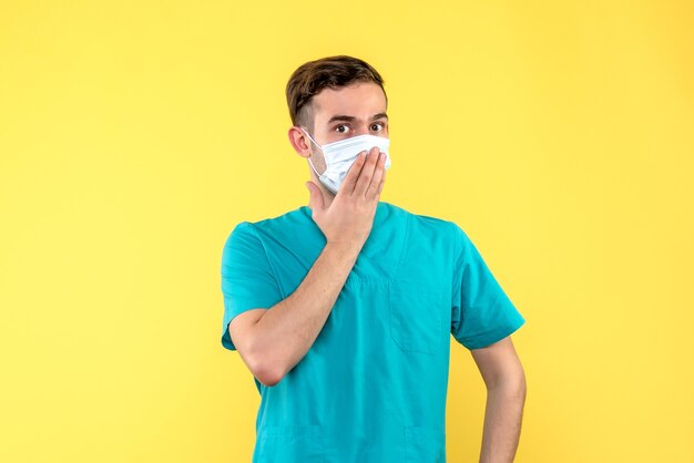 Front view of male doctor in mask on light yellow wall