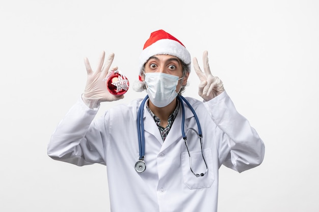 Front view male doctor in mask with toy on a white wall health virus covid new year