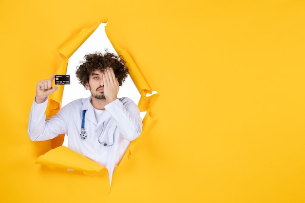 Free photo front view male doctor in medical suit holding bank card on yellow color medicine hospital disease virus medic