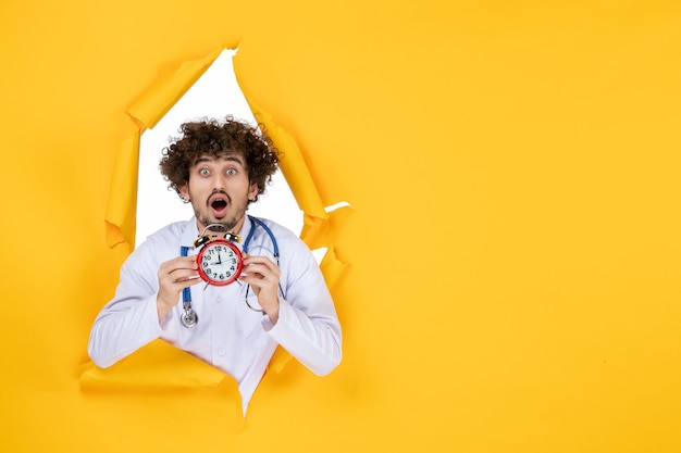 Free photo front view male doctor in medical suit holding clocks on a yellow health color hospital medic shopping medicine time