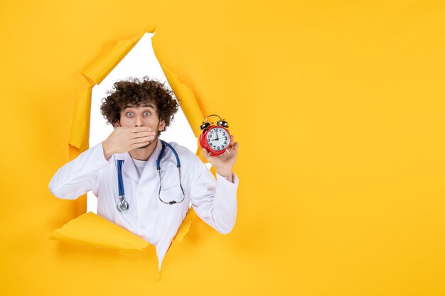 Front view male doctor in medical suit holding clocks on yellow health hospital medic shopping medicine time