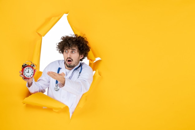 Front view male doctor in medical suit holding clocks on yellow medicine color medic health time hospital virus