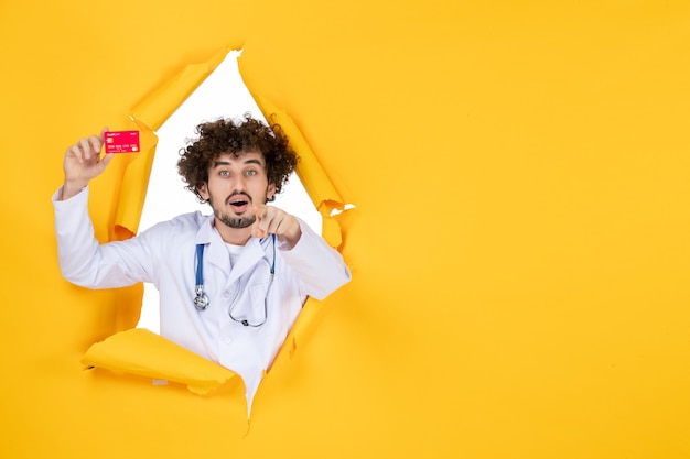 Front view male doctor in medical suit holding red bank card on yellow color medicine hospital disease virus medic health