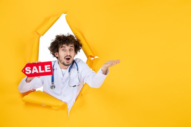 Free Photo front view male doctor in medical suit holding red sale writing on yellow medic color health disease shopping hospital medicine