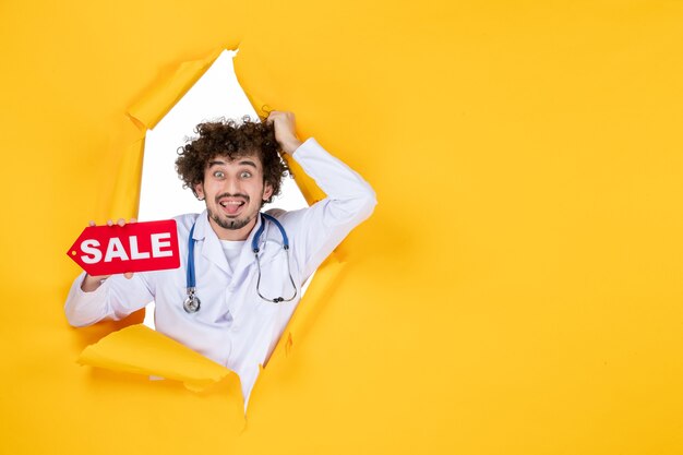 Free Photo front view male doctor in medical suit holding sale writing on a yellow color shopping medic health hospital medicine