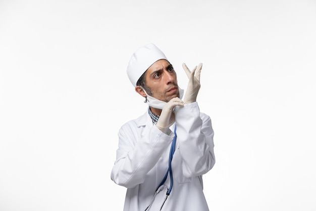 Free photo front view male doctor in medical suit and mask due to coronavirus wearing gloves on a white surface