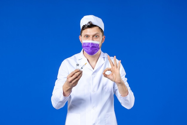 Free photo front view of male doctor in medical suit and mask with injection and vaccine on blue