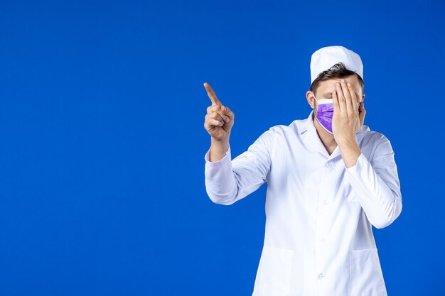 Front view of male doctor in medical suit and purple mask on blue 