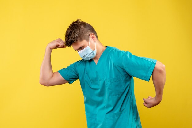 Front view of male doctor in medical suit and sterile mask on a yellow wall