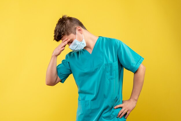 Front view of male doctor in medical suit and sterile mask on a yellow wall