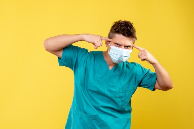 Front view of male doctor in medical suit and sterile mask on yellow wall