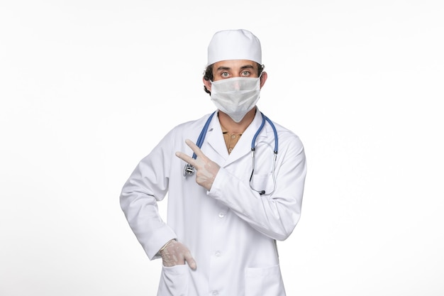 Front view male doctor in medical suit wearing his mask against coronavirus on white desk coronavirus virus pandemic medicine