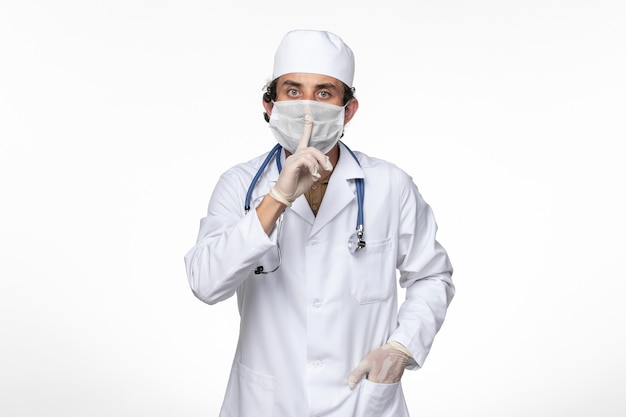 Front view male doctor in medical suit wearing sterile mask as a protection from covid- on light white wall virus illness covid pandemic disease