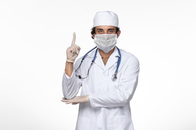 Front view male doctor in medical suit wearing sterile mask as a protection from covid- on white wall virus illness covid- pandemic