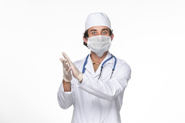 Front view male doctor in medical suit with mask as a protection from covid on white wall coronavirus virus pandemic medicine