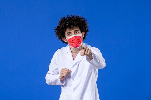 Front view male doctor in medical suit with red mask on blue