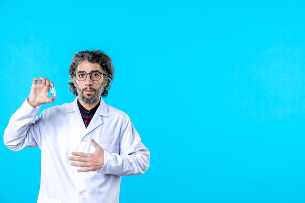 Free photo front view male doctor in medical uniform holding little flask on blue