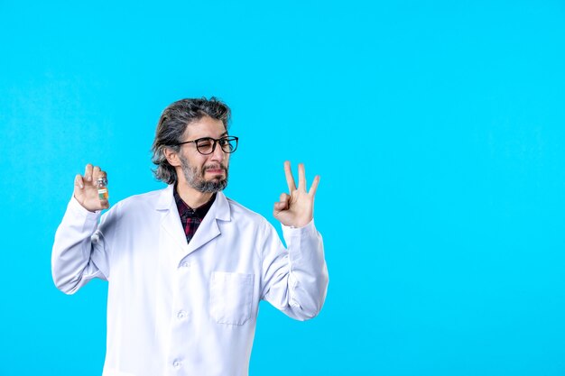 Free photo front view male doctor in medical uniform holding little flask on blue