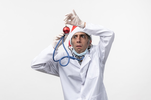 Free photo front view male doctor observing toy on the white wall virus covid health new year