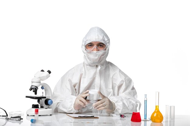 Front view male doctor in protective suit holding empty flask and writing on white desk