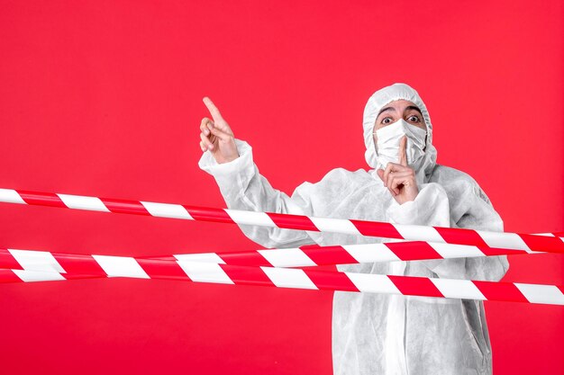 Front view male doctor in protective suit and mask on a red background health cure hospital covid- quarantine color virus isolation